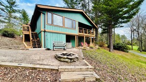 A two-story house with a porch, a fire pit, and a wooden staircase. - NEW Papa's Place on 1st hole Linville Land Harbor Pet Friendly  (Newland)
