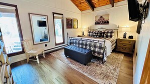 A bedroom with a bed, a chair, a bench, a dresser, a mirror, and a painting on the wall. - NEW Papa's Place on 1st hole Linville Land Harbor Pet Friendly  (Newland)