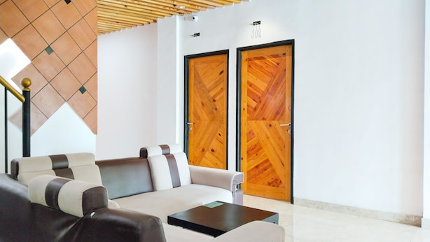 A modern lobby with a sofa, a coffee table, and two wooden doors. - Yayah Guest House Syariah by Cocotel (Dramaga)