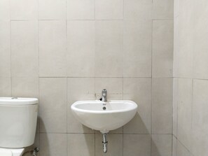 A bathroom with a white toilet and sink, tiled walls, and a visible pipe. - Yayah Guest House Syariah by Cocotel (Dramaga)
