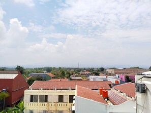 A residential area with red-tiled roofs, some buildings with balconies, and a clear sky with scattered clouds. - Yayah Guest House Syariah by Cocotel (Dramaga)