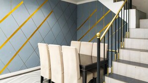 A dining area with a table and chairs, a staircase with a black and gold railing, and a blue wall with diagonal gold lines. - Yayah Guest House Syariah by Cocotel (Dramaga)