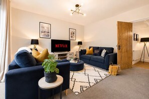 Ein modernes Wohnzimmer mit einem dunkelblauen Sofa, einem runden Couchtisch und einem Flachbildfernseher, der 'NETFLIX' anzeigt.