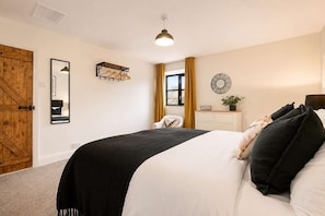 A bedroom with a large bed, a wooden door, a mirror, a wall-mounted fan, and a window with curtains.