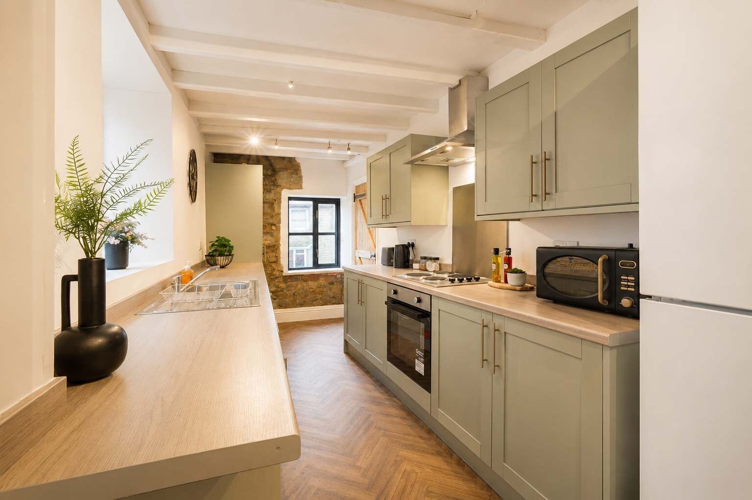 Une cuisine moderne avec des meubles en bois clair, un îlot central et un mur d’accent en pierre.