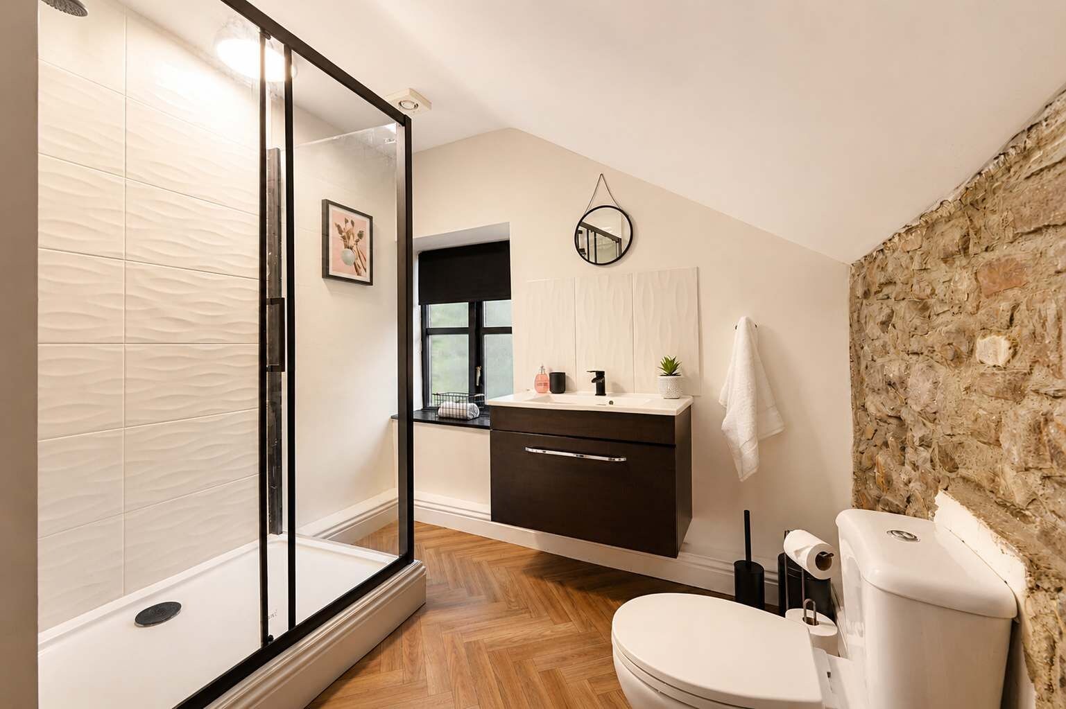 A modern bathroom with a glass shower enclosure, a dark wooden vanity, and a stone accent wall.