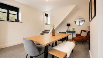 Un espace repas moderne avec une table en bois, des chaises grises, un banc et un vase de fleurs.