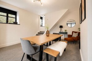 A modern dining area with a wooden table, grey chairs, a bench, and a vase of flowers.