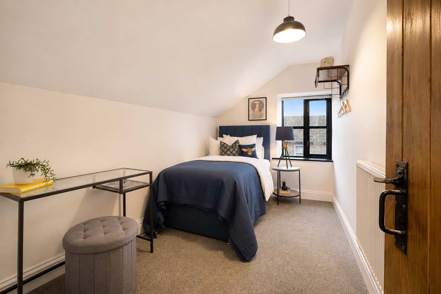 A bedroom with a bed, a bedside table, a lamp, a radiator, a window, and a door.