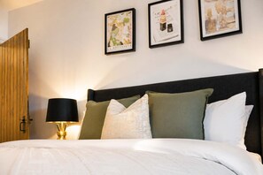 A neatly made bed with a dark headboard, a bedside lamp, and three framed pictures on the wall.