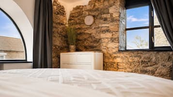 A bedroom with a stone wall, a bed, a dresser, a clock, and a window with curtains.