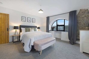 A bedroom with a bed, bedside tables, a bench, a window with curtains, and a stone wall. - Detached three Bedroom Family Home Hot Tub Stay (Bowes)