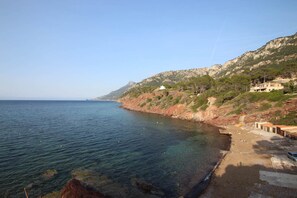A coastal scene with clear water, rocky cliffs, and buildings on the hillside. - Villa Capllonch (Port des Canonge)