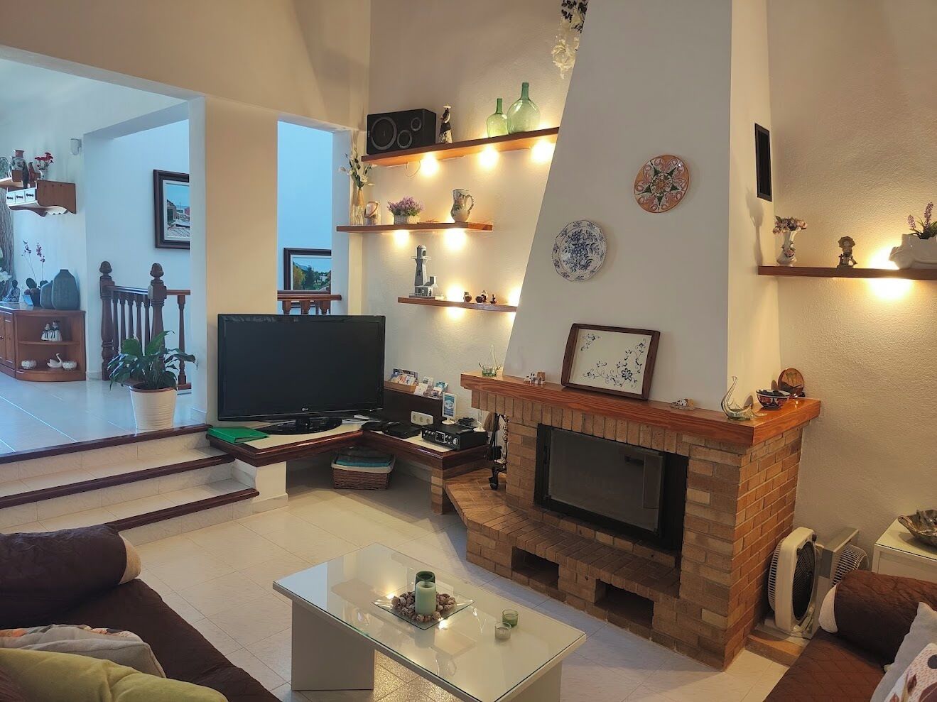 Een woonkamer met een open haard, televisie en planken met decoratieve objecten.