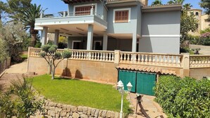 Une maison à deux étages avec un balcon, un mur en pierre et un portail vert.