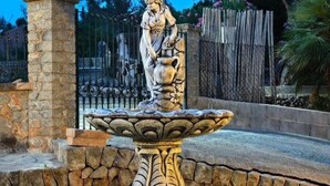 Une fontaine en pierre ornée d’une statue, entourée d’un mur de pierre et d’une clôture en métal.