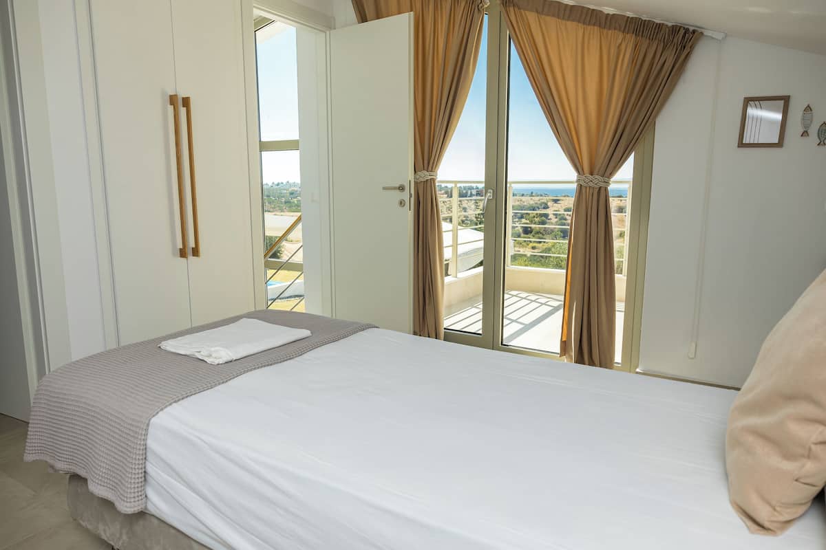 Een slaapkamer met een bed, een raam met gordijnen, uitzicht op het landschap en een deur met een handgreep.