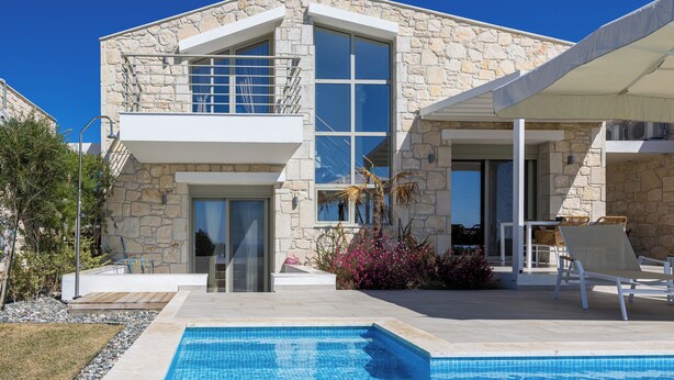 Una casa moderna de dos pisos con fachada de piedra, una piscina y zona de estar exterior.
