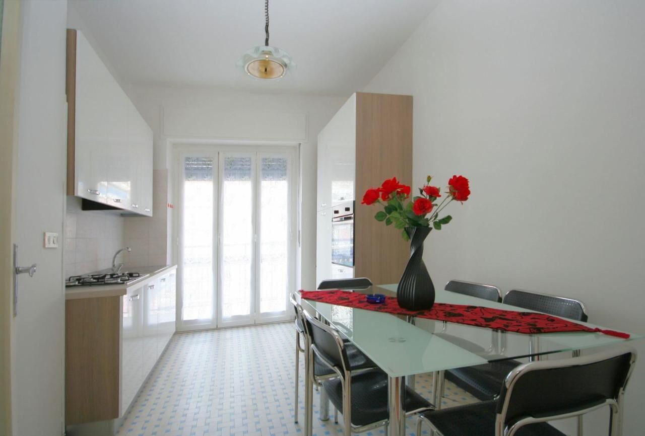 A compact kitchen with a dining area, a large window, and a vase with red flowers on the table.