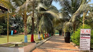A pathway lined with palm trees and a sign indicating the Raj Resort's amenities including parking, reception, dining hall, residence, swimming pool, and wash room. - Raj Resort (Palghar)