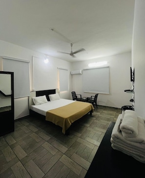 A hotel room with a bed, a desk, a chair, a mirror, a ceiling fan, and an air conditioning unit.