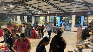 A buffet setup with various food items and people serving and eating. - Raj Resort (Palghar)