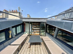 A rooftop terrace with a wooden deck, a bookshelf, and a satellite dish.