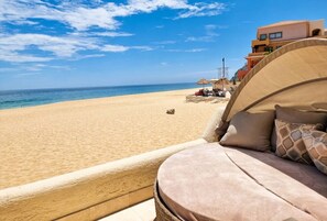 A beach view from a room with a cushioned seating area, a clear sky, and a sandy beach in the background. - Unit 135 - Beachfront Heaven Ocean Front at Terrasol (Cabo San Lucas)