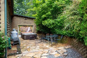 Un patio de piedra con jacuzzi, mobiliario exterior y una cabaña de madera.