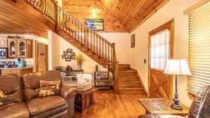 A cozy living room with a leather sofa, wooden staircase, and a kitchen in the background. - Escape to the Dulce Mountain Cabin in Bryson City, NC (Bryson City)
