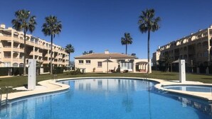 Una piscina rodeada de palmeras y un edificio con varios balcones.