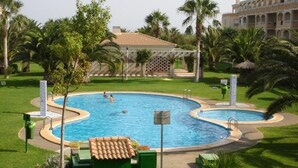 A pool area with a tiled roof, palm trees, and a building in the background.