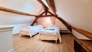 Une chambre mansardée chaleureuse avec deux lits, des poutres apparentes et une commode blanche.