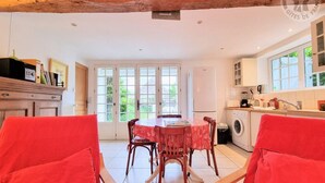 Un coin repas avec une table et des chaises, une cuisine équipée d’un lave-linge et une grande fenêtre donnant sur un paysage verdoyant.