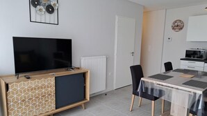 Una sala moderna con un televisor de pantalla plana sobre un mueble de madera, una mesa de comedor con sillas y una puerta blanca.