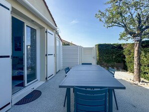 A covered patio with a table and chairs, a sliding glass door, and a hedge.