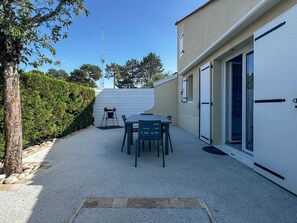Een terras met een tafel en stoelen, een barbecue en een witte deur met raam.