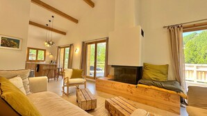 Un salon spacieux doté d’une cheminée, de meubles en bois et de grandes fenêtres offrant une vue sur la verdure.