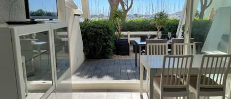 A patio area with a dining table and chairs, a television mounted on the wall, and a view of the sea with sailboats.