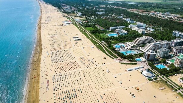 An aerial view of a beach resort with multiple hotel buildings, a sandy beach, and a pool area.