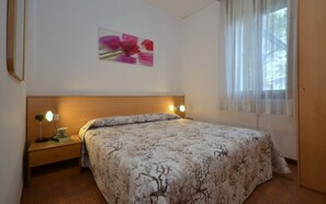 Un dormitorio con una cama, dos mesitas de noche, una lámpara de noche, un cuadro en la pared y una ventana con cortinas.