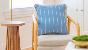 Una habitación con una silla de madera, una mesa redonda de madera, una lámpara de pie blanca y una estantería con adornos.