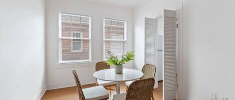 A room with a round table, four wicker chairs, a potted plant, and two windows with blinds.