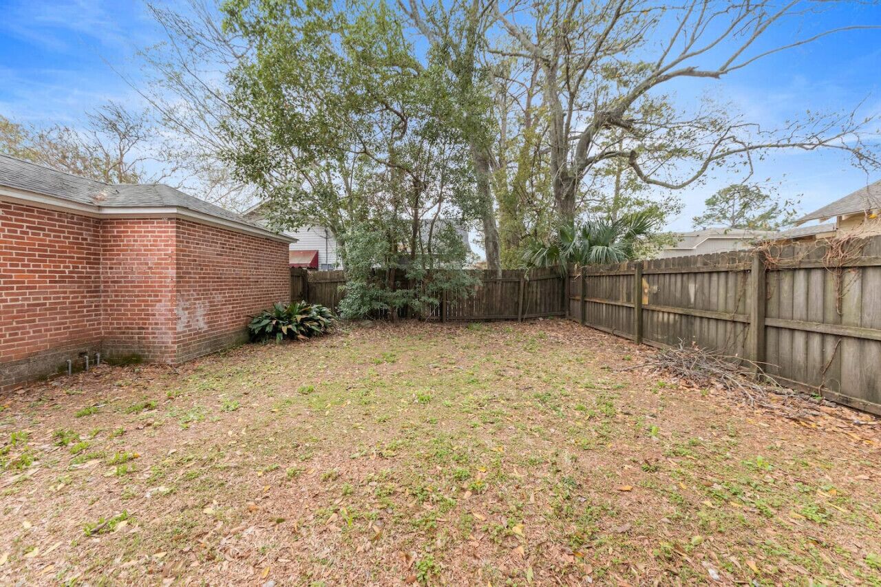 A backyard with a brick wall, a wooden fence, and a large tree.