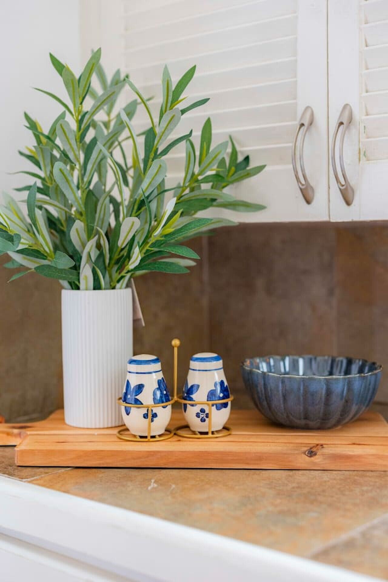 A kitchen counter with a white vase containing green foliage, two ceramic salt and pepper shakers, and a blue ceramic bowl.