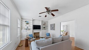Una sala de estar moderna con un sofá blanco, dos sillones, una mesa de centro, un televisor y una chimenea.