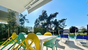 An outdoor seating area with a pool, surrounded by trees and a building in the background. - Golden Hour Retreat Lagoon View Villa With Pool (Rosolina)