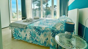 A modern bedroom with a large bed, a bedside table, a lamp, and a view of the outdoors through large windows. - Golden Hour Retreat Lagoon View Villa With Pool (Rosolina)