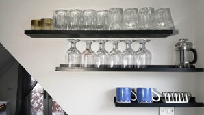 Une pièce avec deux étagères où sont rangés divers objets en verre, une machine à café et une prise électrique.