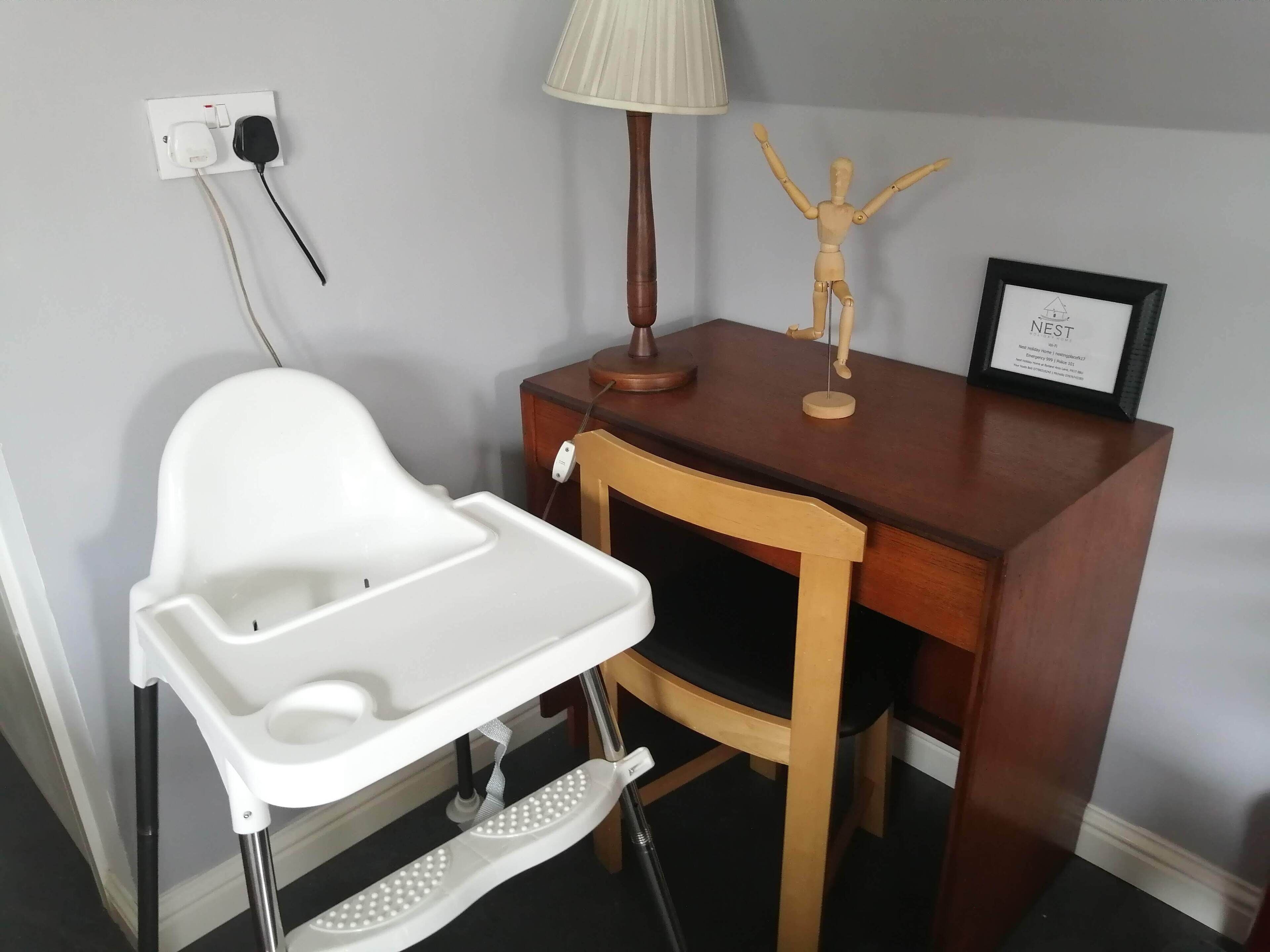A room with a wooden desk, a white high chair, a lamp, and a framed picture on the desk.